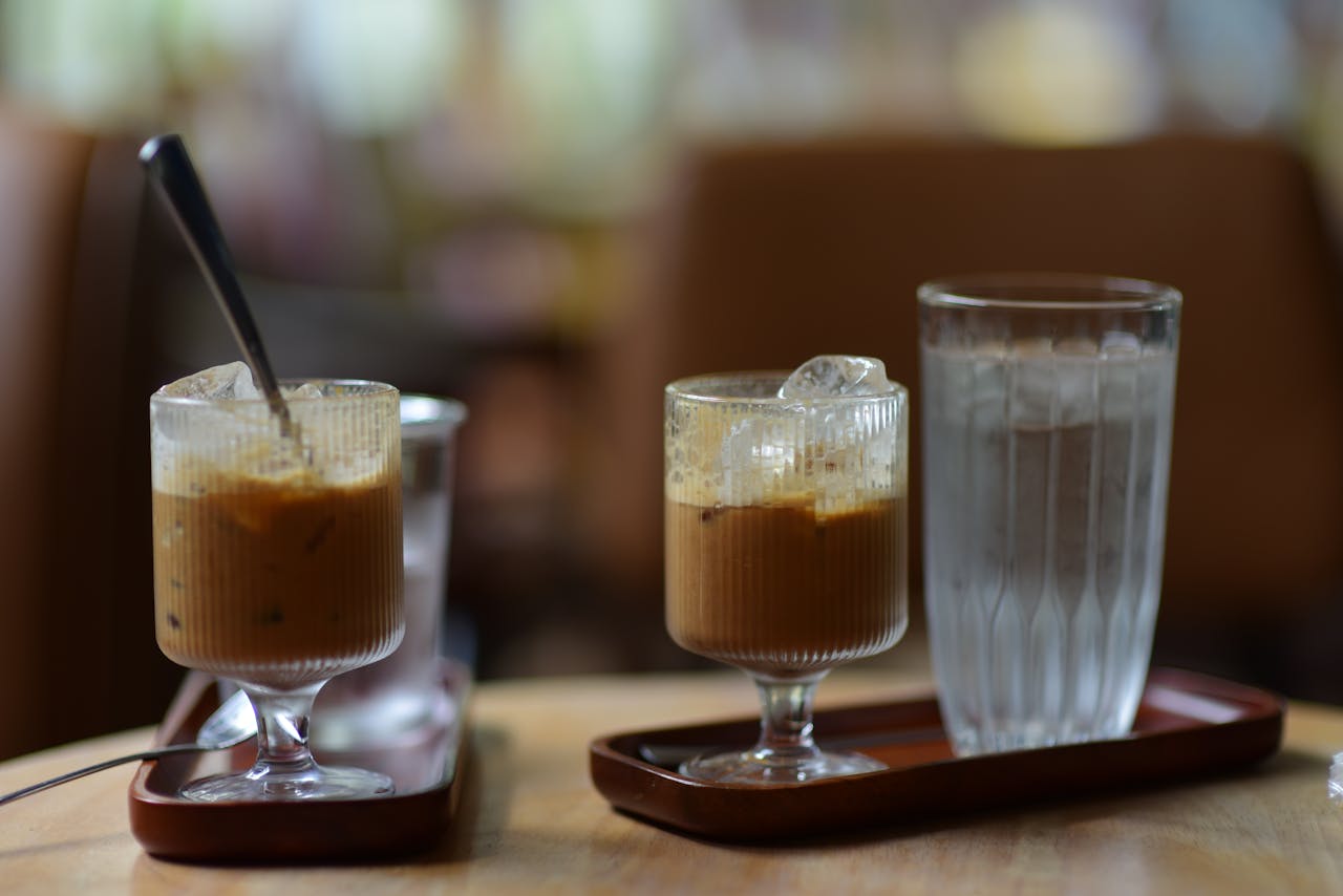 Iced coffee and water in glass tumblers on a wooden table indoors, creating a calm atmosphere.