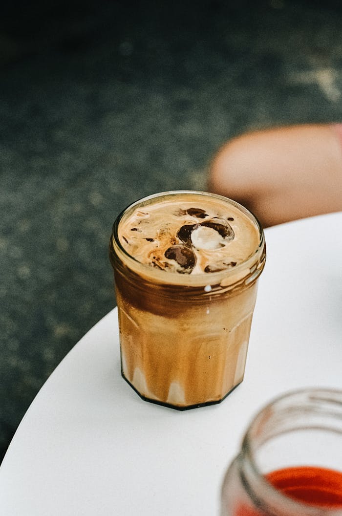 A delicious iced coffee in a jar with ice cubes on a white table outdoors.